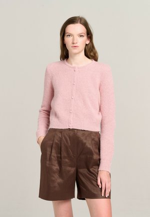 Rosa gestrickte Strickjacke mit langen Ärmeln und runder Halslinie, mit Knopfleiste vorne, getragen über braunen faltigen Shorts.