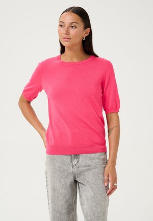 Pink short-sleeve sweater with a round neck, made from a smooth material, featuring ribbed hem and cuffs, worn with light grey pants.