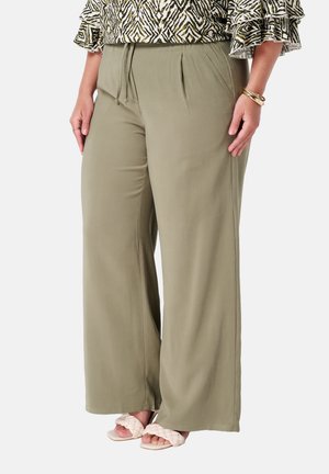 Pantalons larges en tissu vert olive, dotés d'une taille à cordon de serrage et de plis, associés à des sandales tressées en beige clair.