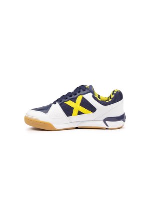 Zapatilla deportiva de corte bajo con malla blanca y azul marino, detalles amarillos, suela de goma y cordones, vista desde el lado exterior sobre fondo blanco.