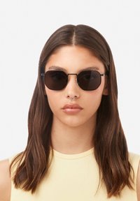 Ümmargused mustad päikeseprillid tumedate läätsedega ja õhukese metallraamiga. Omavad kaheksanurkset kuju ja minimalistlikke riistvaralist detaile.