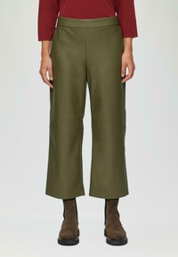 Olijfgroene, brede leren broek met een hoge taille en subtiele textuur, gecombineerd met bruine enkellaarsjes met een dikke zool.