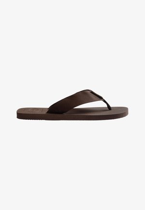 Braune Flip-Flop-Sandale mit strukturierter Sohle und breitem Stoffriemen, flache Sohle, vor weißem Hintergrund dargestellt.