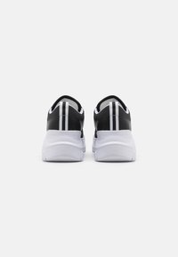 Sneakers pretas com sola branca, apresentando duas riscas brancas verticais na parte de trás, tecido texturizado e um colarinho almofadado para conforto.
