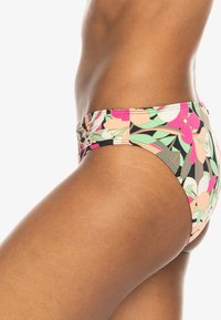 Bas de bikini à motif floral avec un fond noir, présentant des accents roses, pêches et verts. Le matériau semble extensible avec une texture délicate.