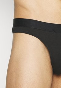 Black cotton brief with a smooth texture and a wide elastic waistband, showcasing a minimalist design and fitted cut.