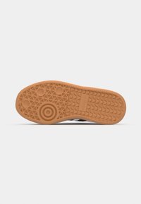 Semelle en caoutchouc d'une basket avec des motifs de bande de roulement géométriques, des dessins circulaires et le logo Adidas embossé au centre.