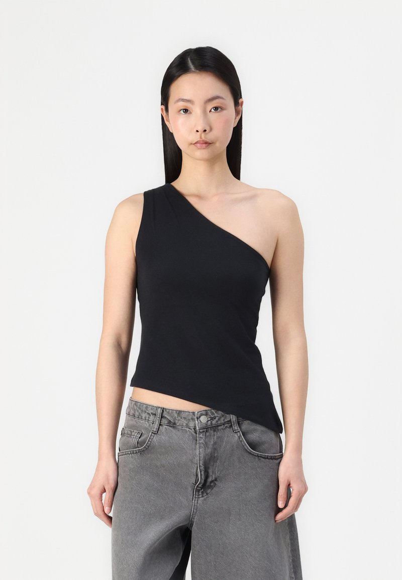 Top negro de un solo lado, hecho de tela suave, con un diseño ajustado y un corte asimétrico en el dobladillo, combinado con unos jeans de pierna ancha en gris claro.