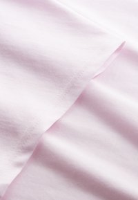 Hellrosa Baumwollstoff mit glatter Textur, einem sauberen Saum und dezenten Nähten. Das Material fällt weich.