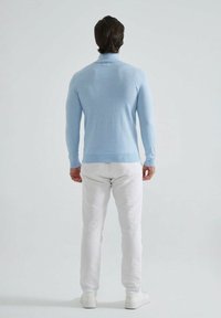 Pull en tricot bleu clair avec un col haut, design ajusté et poignets côtelés, associé à un pantalon slim blanc et des baskets blanches.