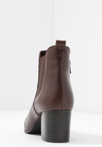 Bottine en cuir marron avec un bout rond, des panneaux latéraux élastiques et un talon noir épais et texturé. Une languette à l'arrière pour un enfilage facile.