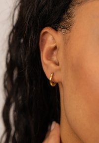 Goldohrringe aus poliertem Metall mit einem runden Design und glatter Oberfläche, die im Ohrläppchen getragen werden.