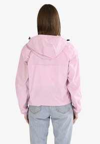 Veste impermeable rose clair avec capuche, poignets élastiques et détail au dos. Design simple avec une texture lisse et brillante.