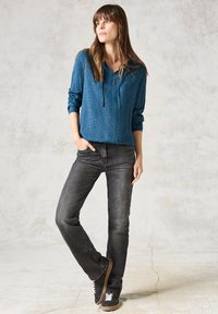 Tealfärgad mönstrad huvtröja med v-ringning och dragsko, kombinerad med utvikt svarta raka jeans och sneakers med brun sula.