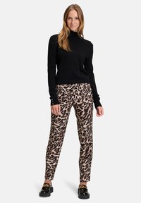 Fekete garbós pulóver bézs és fekete leopárdmintás nadrággal kombinálva. Texturált anyag, amely szoros szabású, arany színű díszgombokkal.