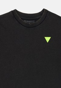 Black organic cotton T-shirt with a round neckline and a textured surface. Features a neon green triangular logo on the front.