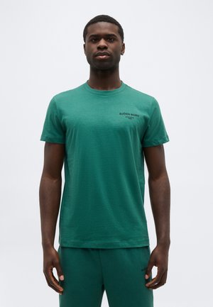 Άνδρας που στέκεται μπροστά, φοράει ένα ταιριαστό πράσινο μπλουζάκι και παντελόνι Björn Borg, με φόντο λευκό.