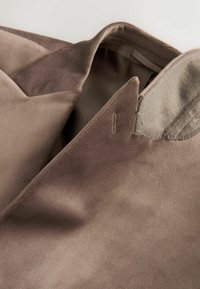 Braunes Wildleder mit einer weichen Textur und glatter Oberfläche. Verfügt über einen Kragen und eine Schulternaht. Subtile Farbvariationen.