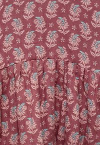 Stoff mit floralem Muster auf maroonfarbenem Hintergrund. Zeigt hellrosa und blaue Blumenmuster, mit gerafftem Detail am Ende.