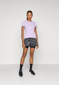 Lys lilla kortermet treningsskjorte med logo; svarte shorts med teksturert mønster; svarte sokker; sporty treningssko.