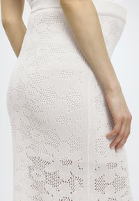 Πλεκτή φούστα μολύβι σε ανοιχτό ροζ, με λουλουδάτο μοτίβο και τμήματα με ανοιχτό πλέξιμο. Φαρδύ ριμπ ζωνάκι και απαλό ύφασμα.