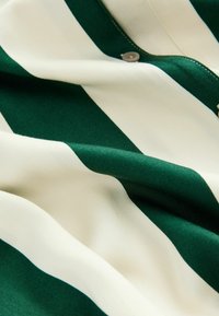 Tissu rayé vert et crème avec une texture douce, comportant une fermeture à bouton et un drapé fluide.