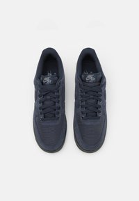 O pereche de teni Nike Air Force 1 de culoare bleu închis, cu şireturi, văzută dintr-o parte de sus pe un fundal alb.