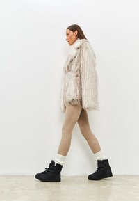 Faux fur-frakke i beige med en struktureret overflade, parret med beige strømpebukser og sorte ankelstøvler med snørebånd samt hvide opsmøgede sokker.