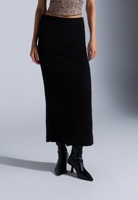 Lange zwarte gebreide rok met een aansluitende tailleband, gedragen met zwarte puntige haklaarzen. Gestructureerde, zachte stof met een gladde afwerking.