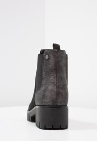 Botín negro con panel trasero texturizado, insertos elásticos en los laterales, lengüeta y suela gruesa de tracción, sobre un fondo blanco.