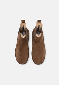 Botas de tobillo de ante marrón con un forro interior suave, paneles laterales elásticos y tiradores para facilitar su uso. Suelas planas con una forma de punta redondeada.