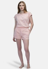 Maglietta rosa con un motivo maculato, abbinata a pantaloni corti rosa coordinati con una cintura elastica e un cordino. Tessuto leggero.