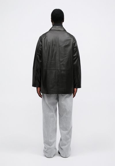 Melna ādas jaka ar brīvu piegriezumu un plašiem pleciem, apvienota ar gaiši pelēkiem brīvi pieguļošiem džinsiem. Gluda faktūra, minimāls dizains.