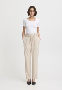 Pantaloni beige a vita alta con cintura legata, tasche laterali, tessuto morbido e vestibilità rilassata abbinati a un top aderente bianco a maniche corte.