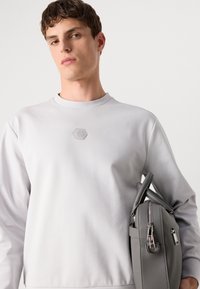 Felpa grigia chiaro con collo rotondo e dettaglio del logo esagonale. Borsa grigia in pelle con cerniere e superficie testurizzata.