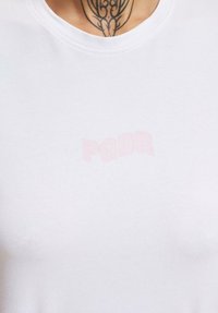 Biele bavlnené tričko s okrúhlym výstrihom, na ktorom je svetloružový nápis "PGDR" vytvorený jemnou, mierne vystúpenou potlačou.