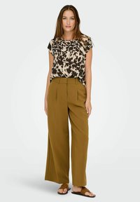 Top a maniche corte con stampa animale marrone e crema; pantaloni a gamba larga verde oliva con pieghe; sandali brown a scivolo, sfondo neutro.