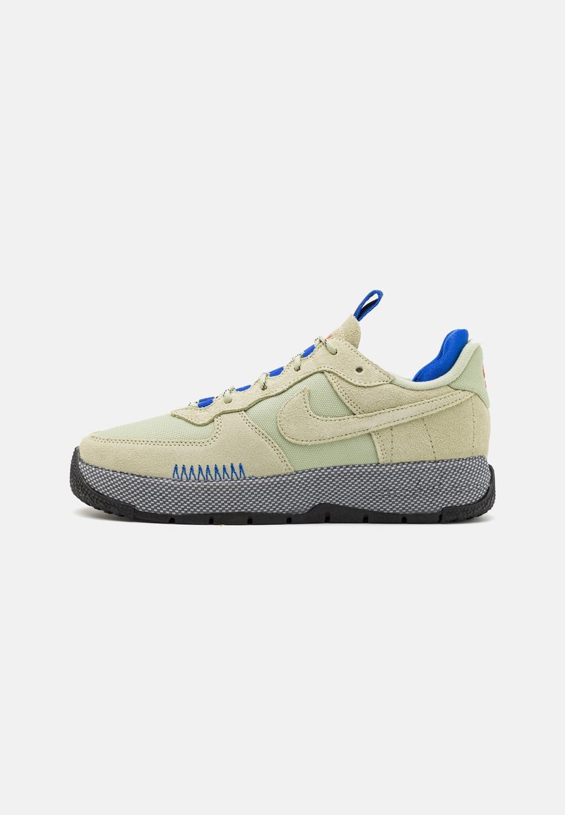 Baskets beige et vert clair avec des touches bleues, semelle texturée gris foncé, dessus en tissu et daim, et logo Nike sur le côté.