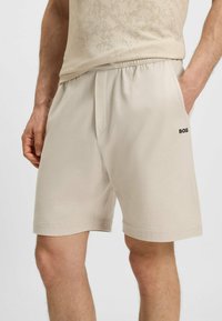 Pantaloni sportivi beige con vita elasticizzata, caratterizzati da una texture perforata e tasche laterali. Logo visibile sull'orlo inferiore.