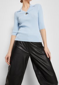 Jasnoniebieski sweter w prążki z kołnierzykiem polo i pojedynczym guzikiem, w połączeniu z czarnymi, skórzanymi, szerokimi spodniami.