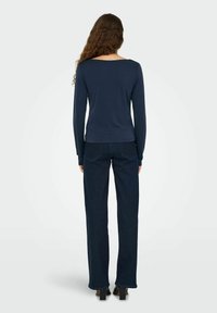 Marineblå langærmet top med bådudskæring, parret med mørkeblå lige ben jeans. Blødt stof og minimalistisk design. Ensfarvet uden mønstre.