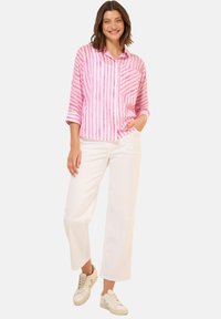 Roze en witte gestreepte blouse, met knopen, met een zak; gecombineerd met witte broek met een wijd been en lichtgekleurde sneakers.