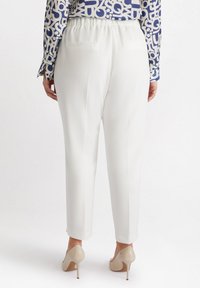 Witte op maat gemaakte pantalon met een ontspannen pasvorm, voorzien van een verhoogde elastische tailleband en twee achterzakken. Draagt met een gestreept blauw overhemd en nude hakken.