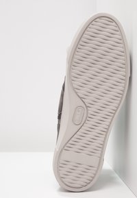 Sneaker grigia in suede con suola in gomma bianca texturizzata. Le caratteristiche includono un design cucito e un dettaglio del logo sul lato.