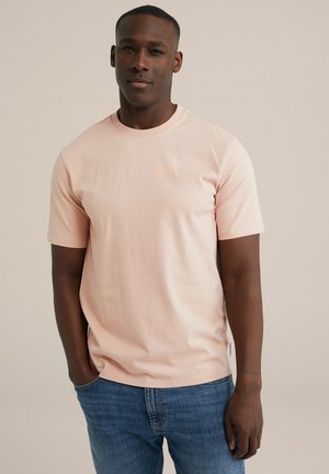Lyserød kortærmet t-shirt i blødt bomuldsstof med rund hals og lige kant, parret med blå denim jeans.