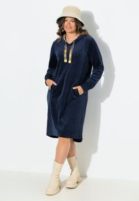 Navy sininen fleece-mekko hupulla, jossa on kukkakuosiset narut ja etutaskut. Yhdistetty vaaleanbeigeihin nilkkasaappaisiin.