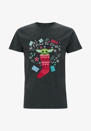 Chemise gris foncé avec un personnage vert qui regarde depuis une chaussette de Noël rouge entourée de cadeaux et de feuillage d'hiver avec le texte « Tout ce que je veux pour Noël ».