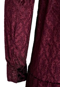 Bordowa bluzka z koronkowymi rękawami, zdobiona misternymi wzorami kwiatowymi, z fakturowanej tkaniny oraz dwiema guzikami na mankiecie.