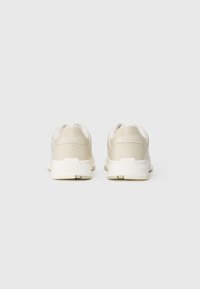 Beige athletic shoes with a smooth synthetic upper, padded collar, and a contrasting white sole, featuring a textured tread pattern.