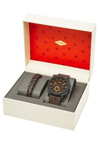 Fossil-horloge met een zwarte kast en een bruine leren band, gecombineerd met een bruine gevlochten armband, gepresenteerd in een crèmekleurige doos met een rode binnenkant.